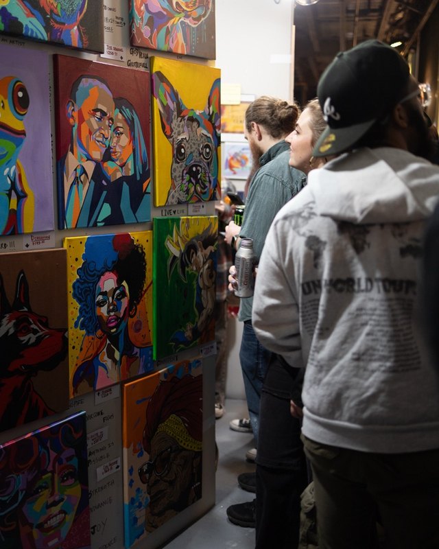 Visitors browsing a wall of colorful paintings at the Pancakes & Booze art show