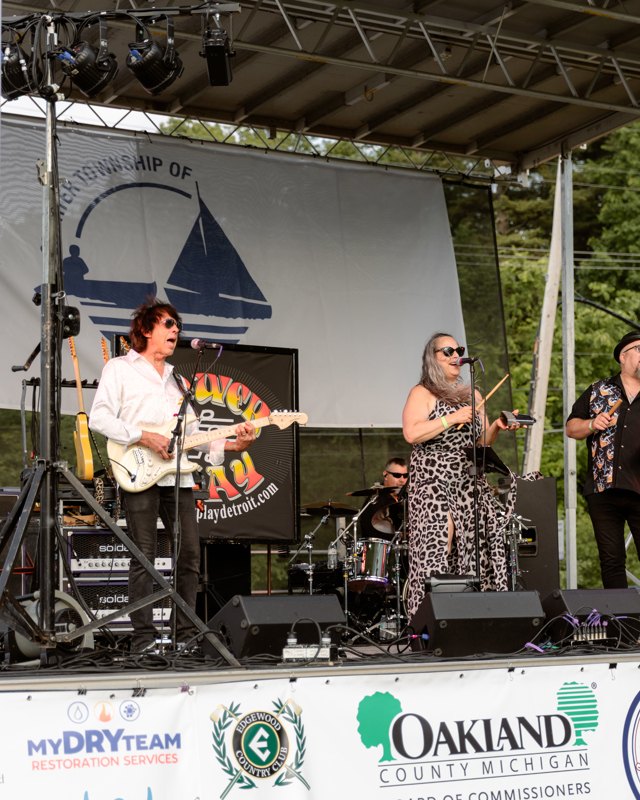 Live band performing on the Heart of the Lakes festival main stage with sponsor banners below.
