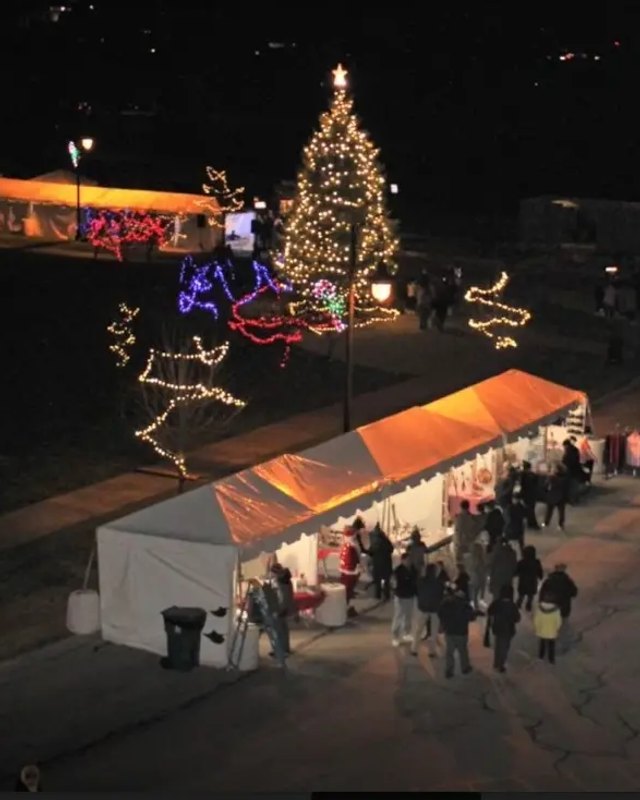 Night view of the Shorewood holiday market with white vendor tents, lit Christmas tree and a crowd walking through