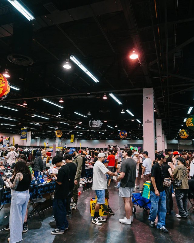 Crowd of shoppers moving through the Sneaker Con show floor with vendor booths and hanging decorations