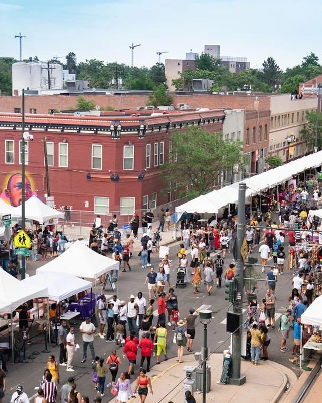 Wide view of a street festival with white vendor tents and a large crowd along a downtown street.