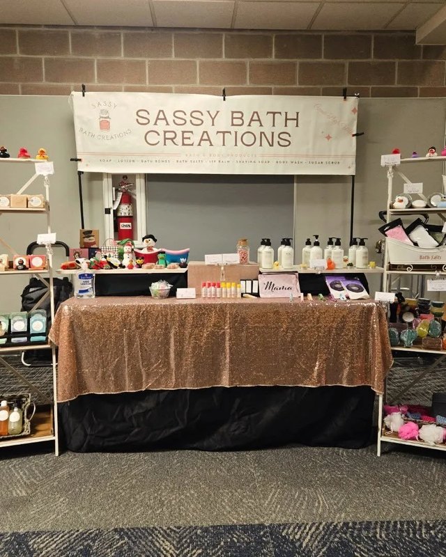 Sassy Bath Creations vendor booth with shelves of bath products under a banner