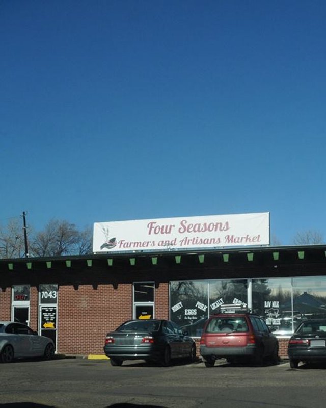 Brick building with a Four Seasons Farmers and Artisans Market sign and parked cars out front.