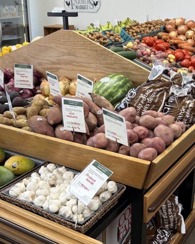 Produce display with potatoes, citrus, avocados, garlic and watermelon on wooden tiered tables at Homestead.Market. The original alt text named apples and squash, which aren't clearly visible.
