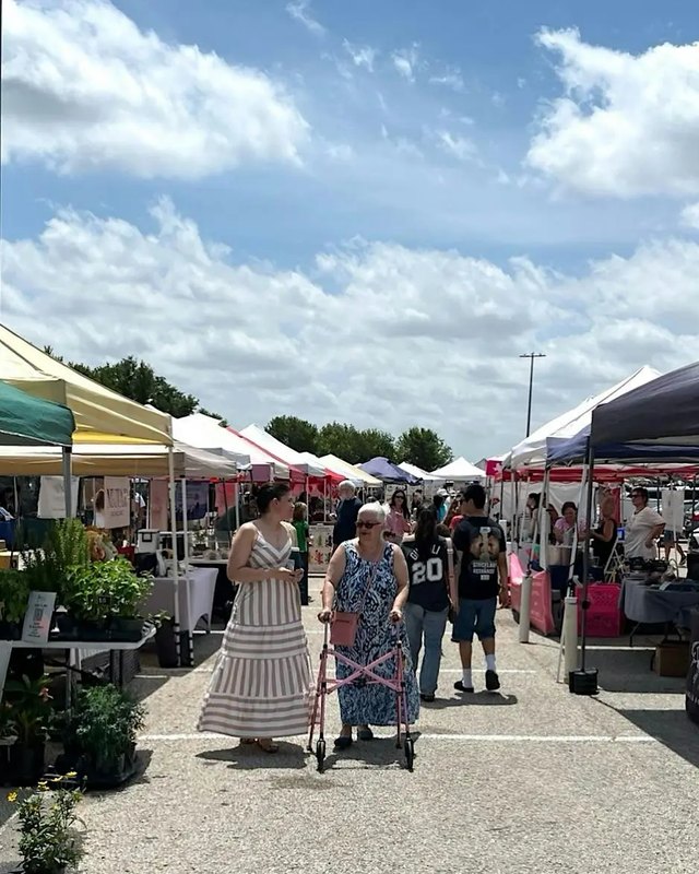 Outdoor market with white and colored canopy booths and shoppers walking between the vendor tents.