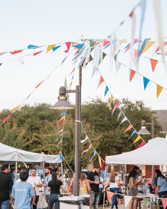 Festival crowd browsing white tents under colorful bunting at an outdoor market.