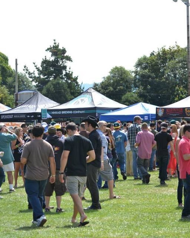 Wide view of a festival crowd walking between white vendor tents on a grass field