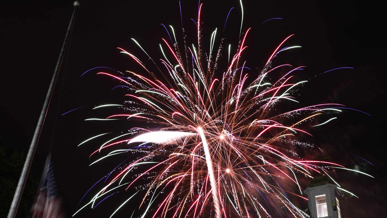 Red, white and green fireworks burst in the night sky above a town building tower.