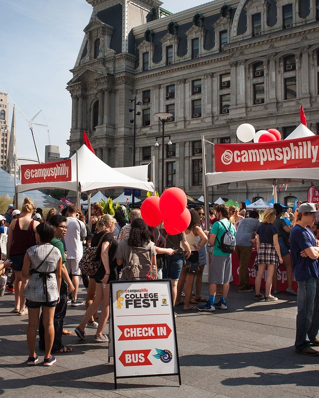 Students crowding around Campus Philly booths with red balloons and a check-in sign outside City Hall.