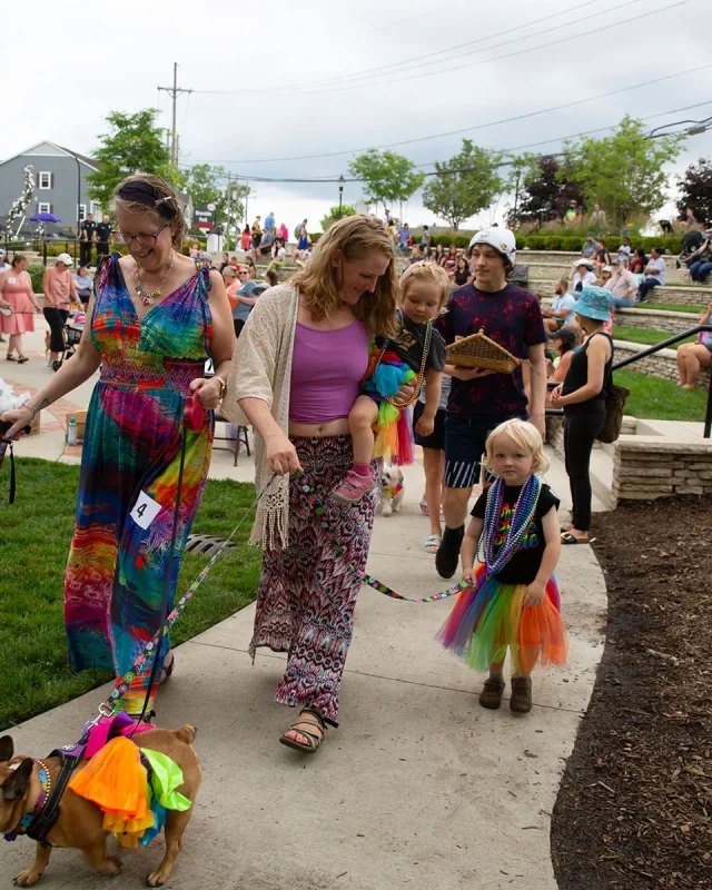 Costumed parade walkers and a dog in a costume on a path with a crowd behind them at Auburn Hills Summerfest.