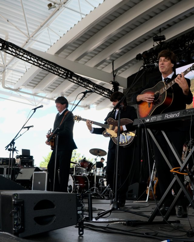 Musicians in dark suits performing on a stage at Polish Fest, with a large screen showing the festival's Polish Fest banner behind them.
