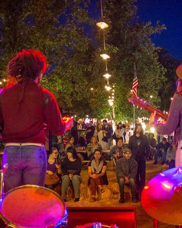 Performer with a drum kit facing a crowd gathered under string lights at an outdoor evening event at Vail Moonlight Markets