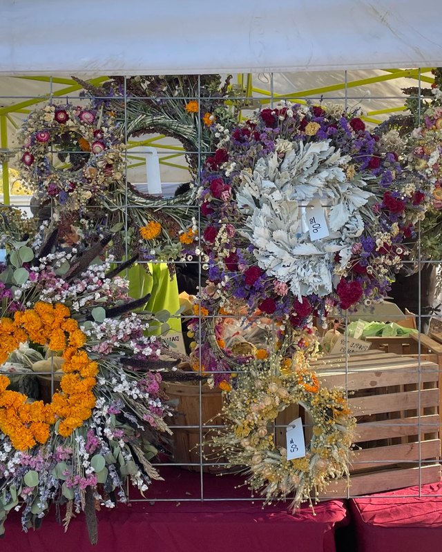 Dried flower and wreath display at a market booth on a red tablecloth.