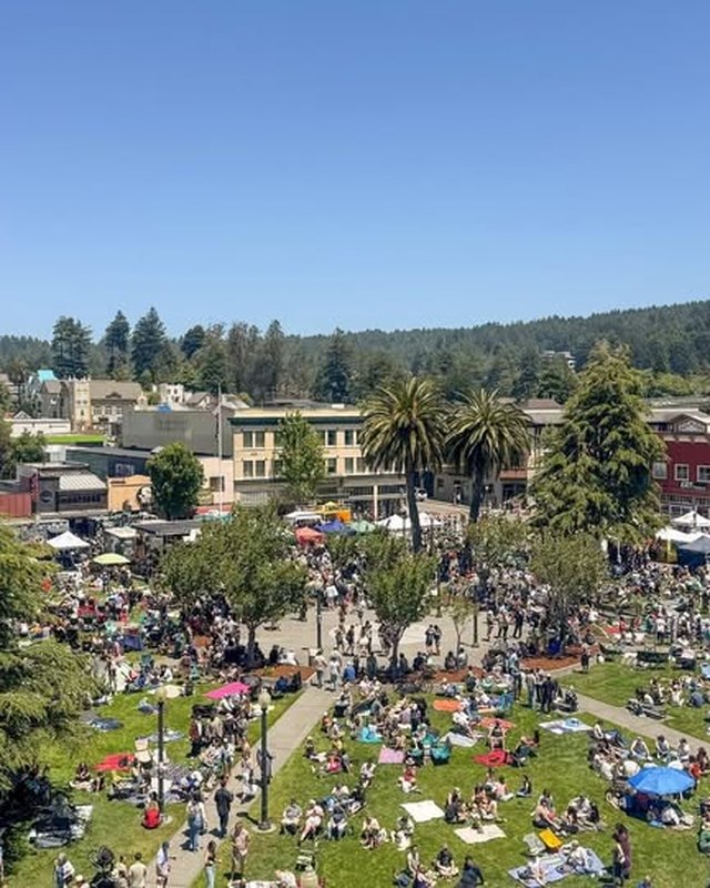 Aerial view of a crowd and white vendor tents on a park lawn ringed by buildings