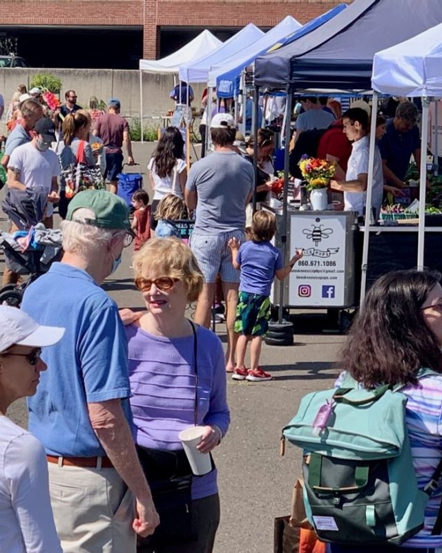 Shoppers and vendors' blue tents at the New Canaan Farmers Market in the Lumber Yard lot.
