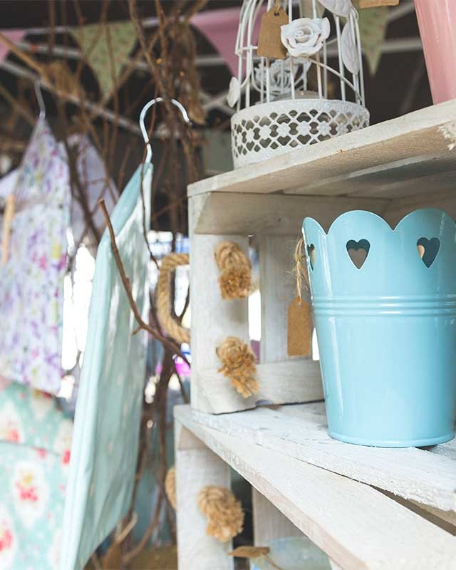 Vintage market stall with a light blue bucket, bunting and rustic wooden shelves holding decor goods.