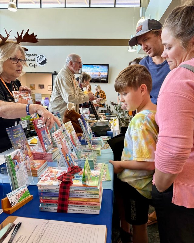 Shoppers browsing a book vendor table with stacked books and a sign-in sheet at the festival.