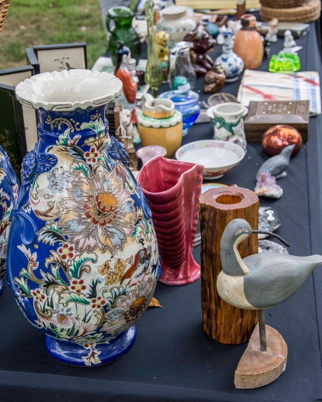 Table of vintage vases, ceramics and carved wooden decoys on display at the flea market.