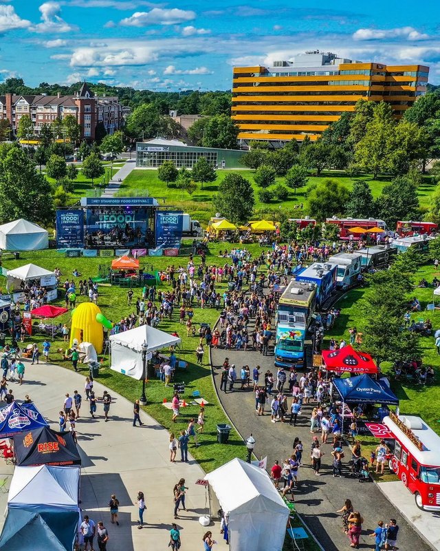Aerial view of the Hey Stamford food festival with food trucks, white tents and crowds on the lawn.