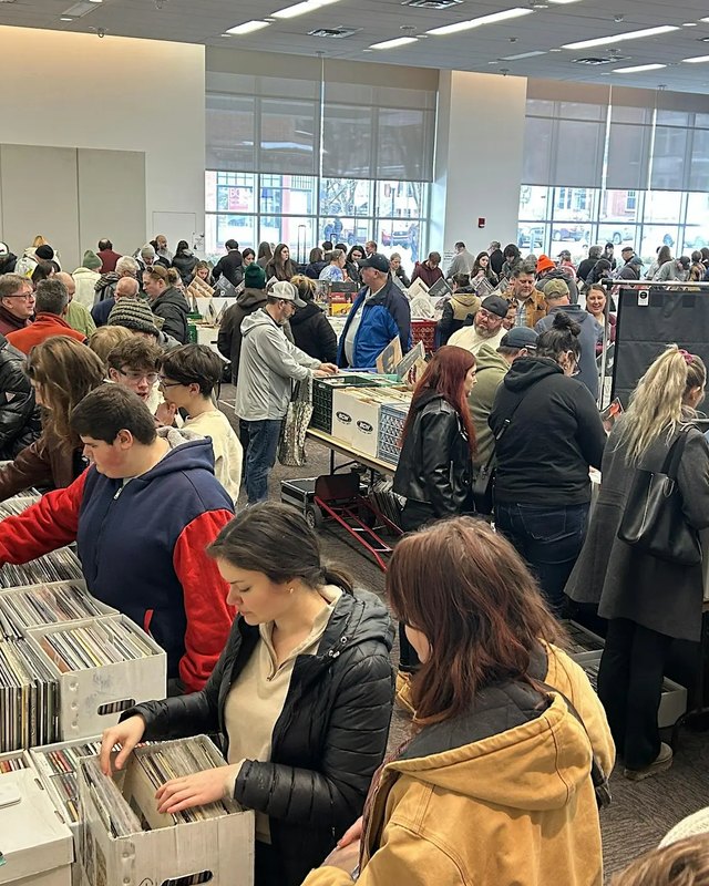 Crowds of shoppers digging through crates of records at a large indoor vinyl sale.