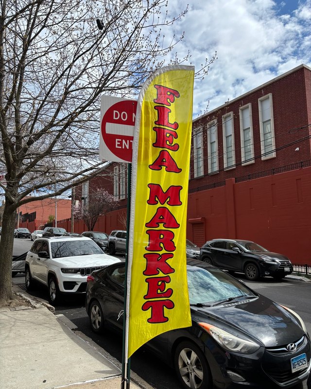 Yellow FLEA MARKET banner flying on a street in front of brick buildings and parked cars.