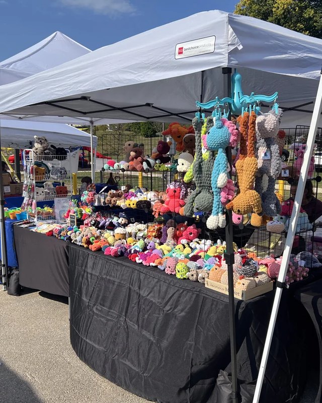 Crafter's booth with stuffed toys and goods on a black-draped table under a white tent at the festival