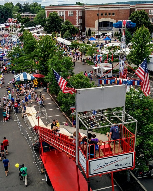 Aerial view of a crowded festival street with white vendor tents, shoppers and a red stage truck.