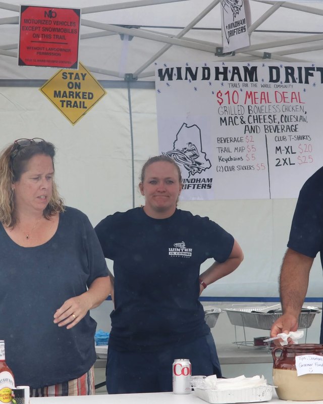 Two volunteers behind the Windham Drifters food booth under a white tent at Windham Summerfest, with a meal-deal sign.