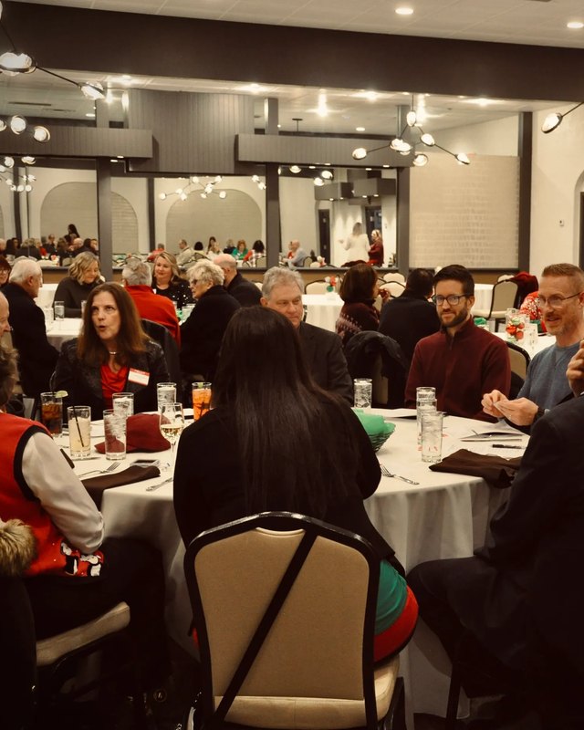Attendees seated at round tables with white cloths and drinks in a banquet hall with hanging lights.