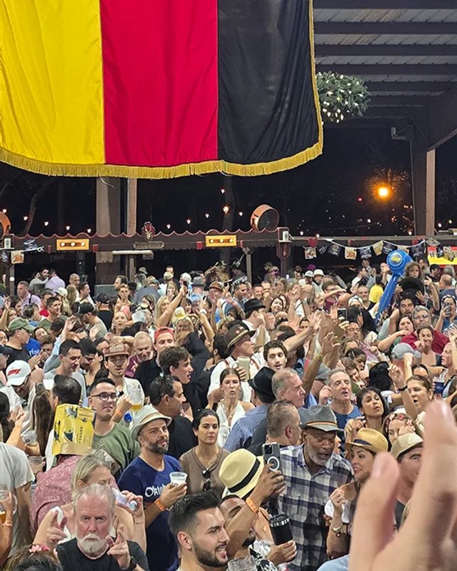 Large crowd with raised hands at the Oktoberfest celebration under a German flag at night.