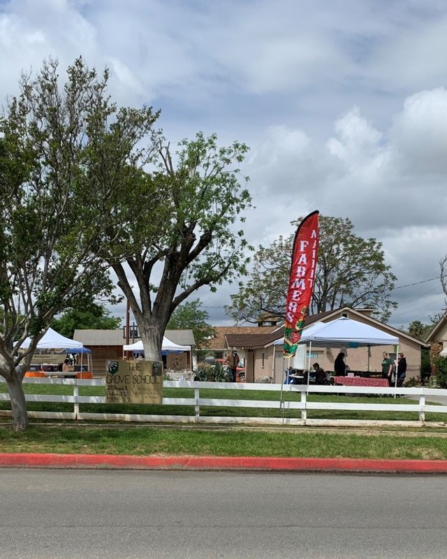 Market tents set up on grass beside a white fence at the Grove School farmers market in Redlands.