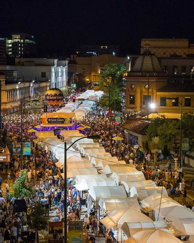 Night aerial view of a crowded street fair with white tent booths and shoppers at the Plaza Art Fair.