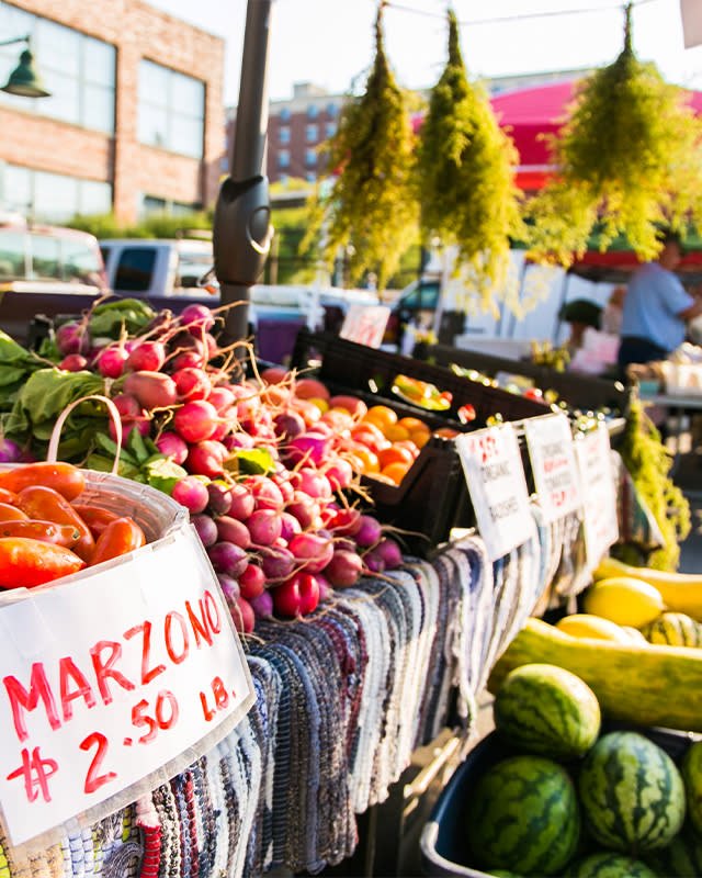 Produce stall with radishes, tomatoes, squash and watermelons at an outdoor market with a $2.50 price sign.