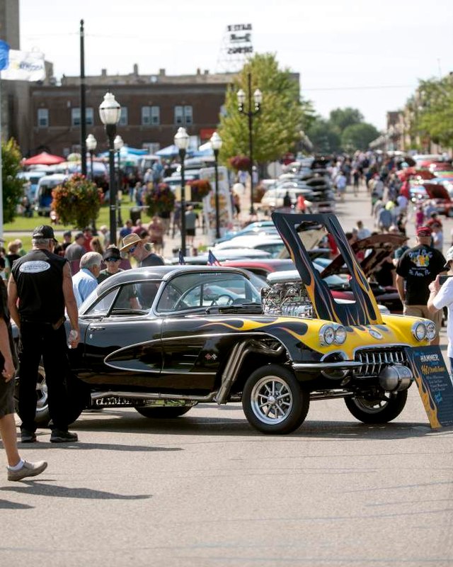 Classic car show crowd on a downtown street with a black custom car and people browsing.