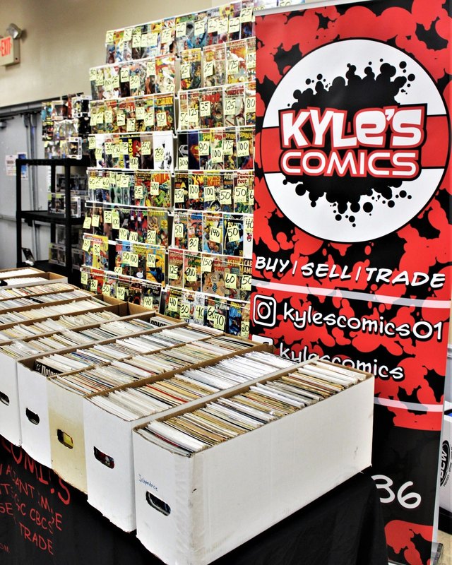 Kyle's Comics vendor display of comic longboxes and a comic wall at a show.