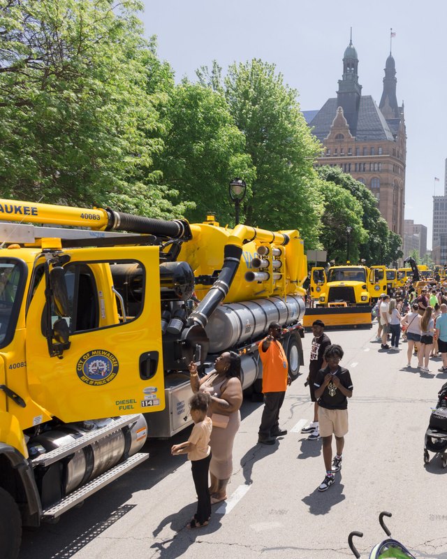 Yellow city trucks lined up on a downtown Milwaukee street with crowds walking between them.