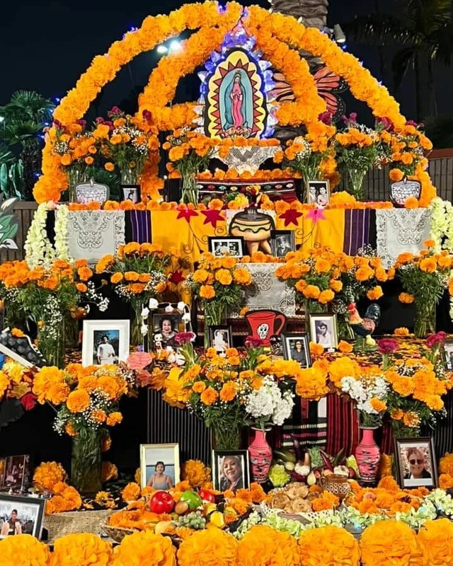 Marigold-covered altar with a Virgin of Guadalupe image and framed photos at a Downey Día de los Muertos festival.