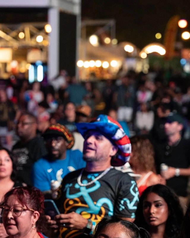 Festival crowd of people gathered at night under string lights, some wearing flags.
