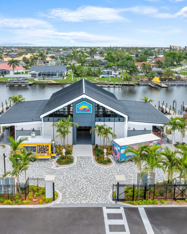 Aerial view of the Slipaway Food Truck Park building and palm-lined grounds beside the waterway, with food trucks visible.