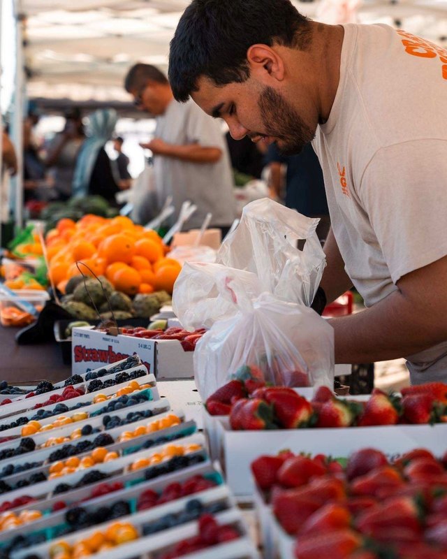Vendor filling a plastic bag with produce at his booth at the Fontana Farmers Market