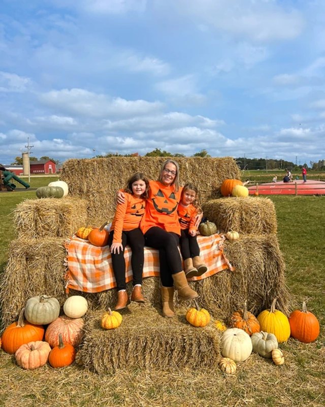 Family sitting on hay bales with pumpkins at the Thompson Farm Fall Festival.