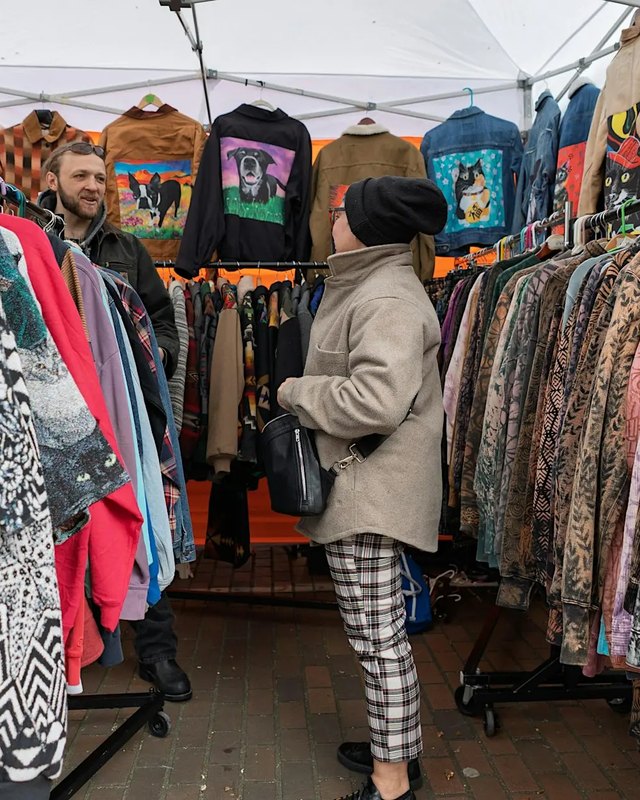 Shoppers browsing clothing racks and vintage garments at a booth under a white tent at Occidental Square.