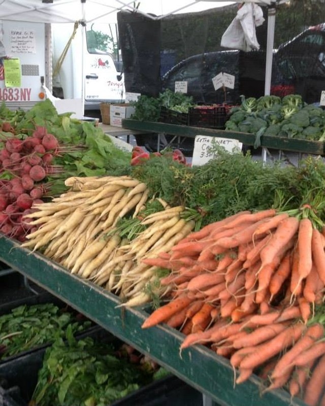 Produce stand at a market with carrots, beets and radishes on display under a white tent.