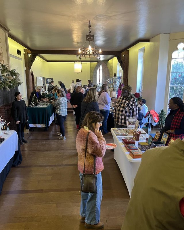 Shoppers browsing vendor tables with goods in a warm wood-floored hall at Cloisters Castle.
