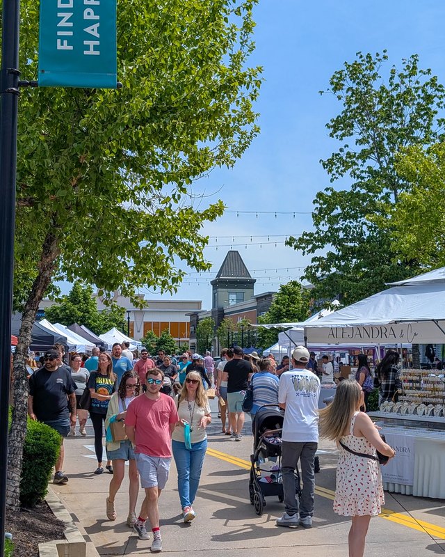 Crowd of shoppers walking past white vendor tents along a sunny outdoor street market at The Avenue