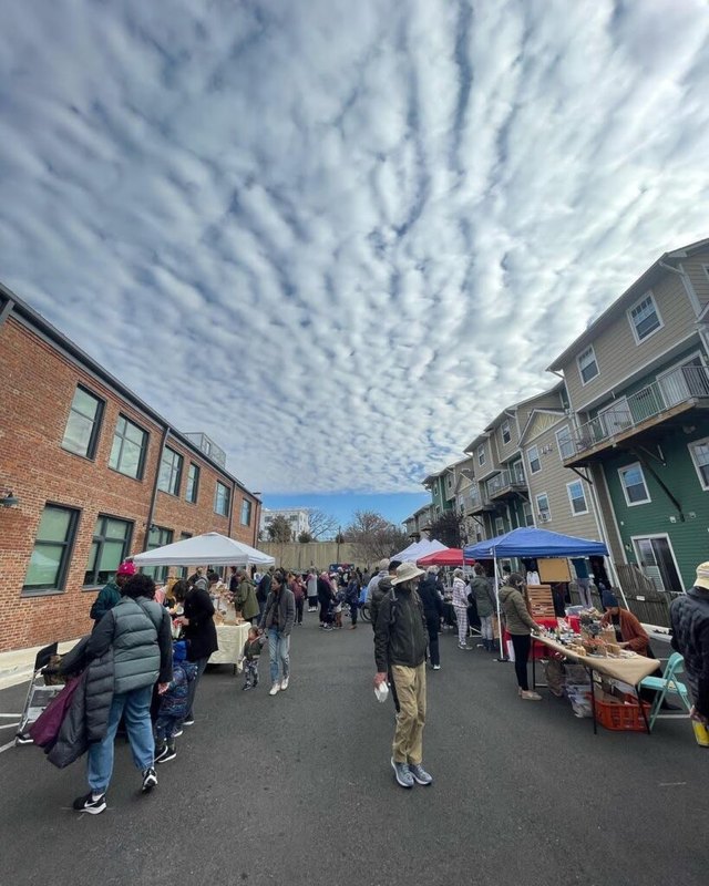 Shoppers walking past market booths on a street under a cloudy sky