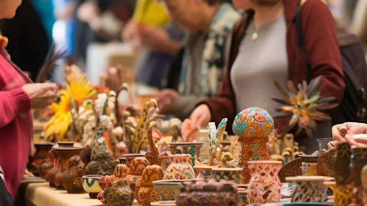 Shoppers browsing handmade crafts and artwork on tables at a market booth.