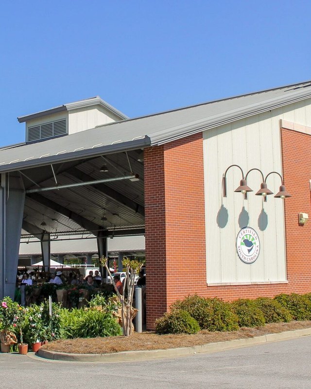 The SC State Farmers Market open-sided brick shed with shoppers and produce stands under its roof.