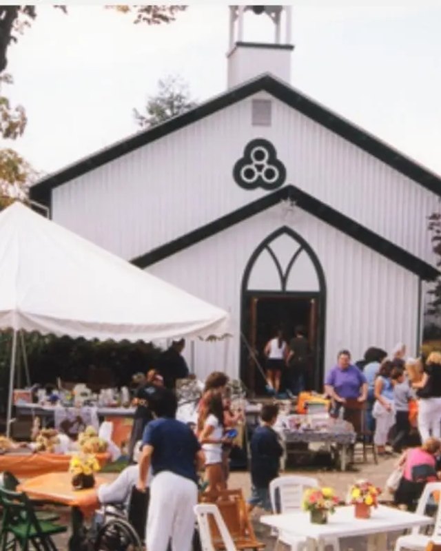 Crowd browsing white tents and tables of goods in front of a white church during Historic Fallsington Day.