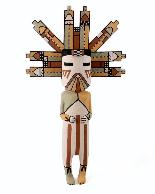 A carved katsina doll with a tall painted headdress standing against a plain white background